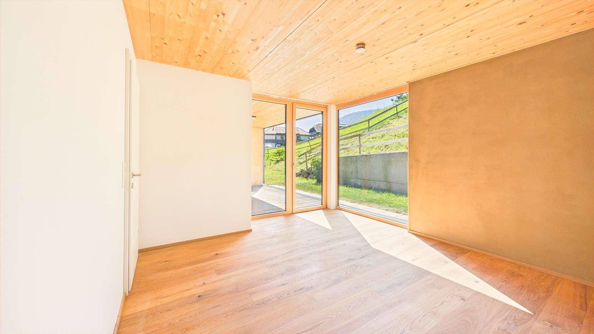 Geräumiges Schlafzimmer mit Holzboden und Holzlamellendecke, bietet durch große Fenster einen weiten Blick.