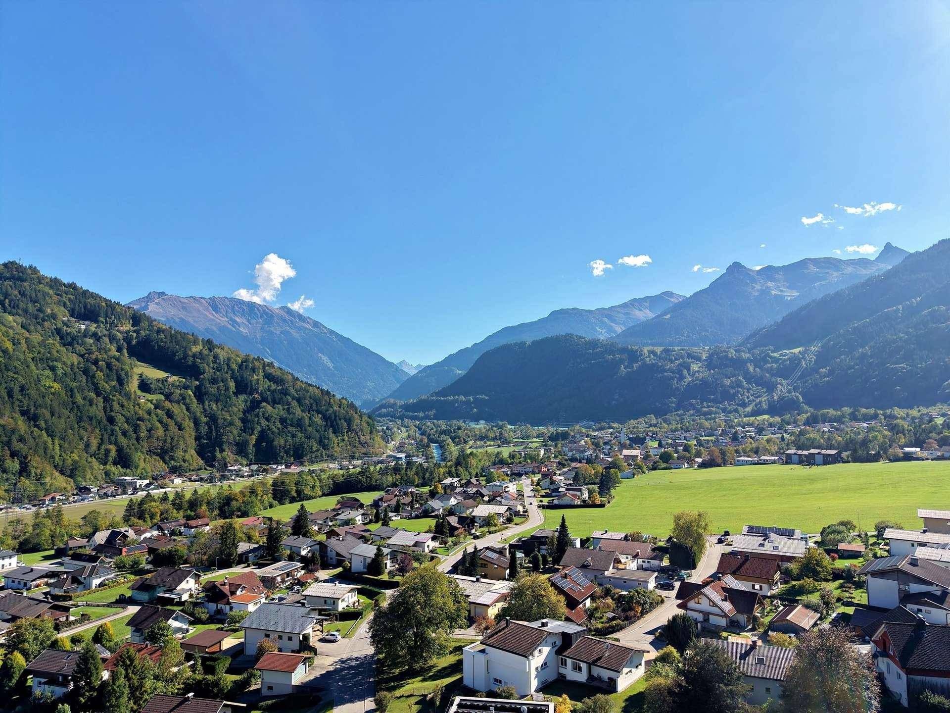 Weitwinkelaufnahme aus der Luft zeigt ein Dorf in einem Tal mit beeindruckender Bergkulisse.