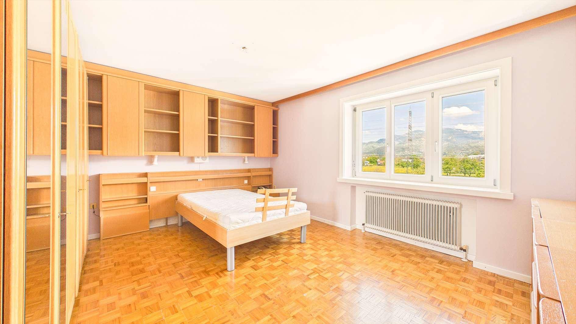 Schlafzimmer mit Einbauschränken, Holzboden und Fenster mit Blick ins Grüne.