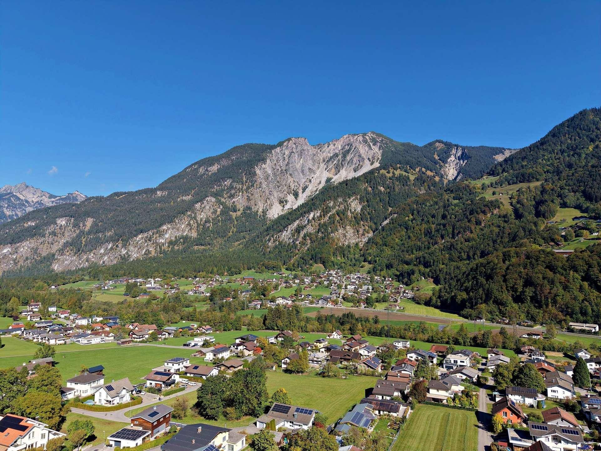Weitläufige Luftaufnahme eines Dorfes eingebettet in eine malerische Berglandschaft.