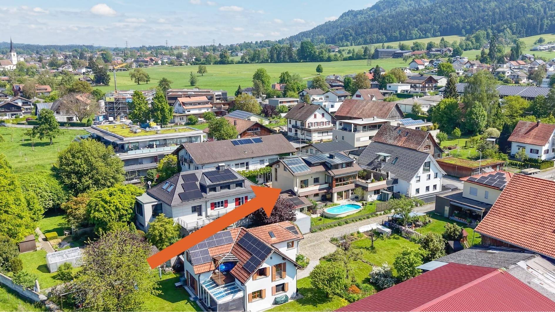 Weitläufige Luftaufnahme der Wohngegend mit Häusern, Gärten und Bergen im Hintergrund.