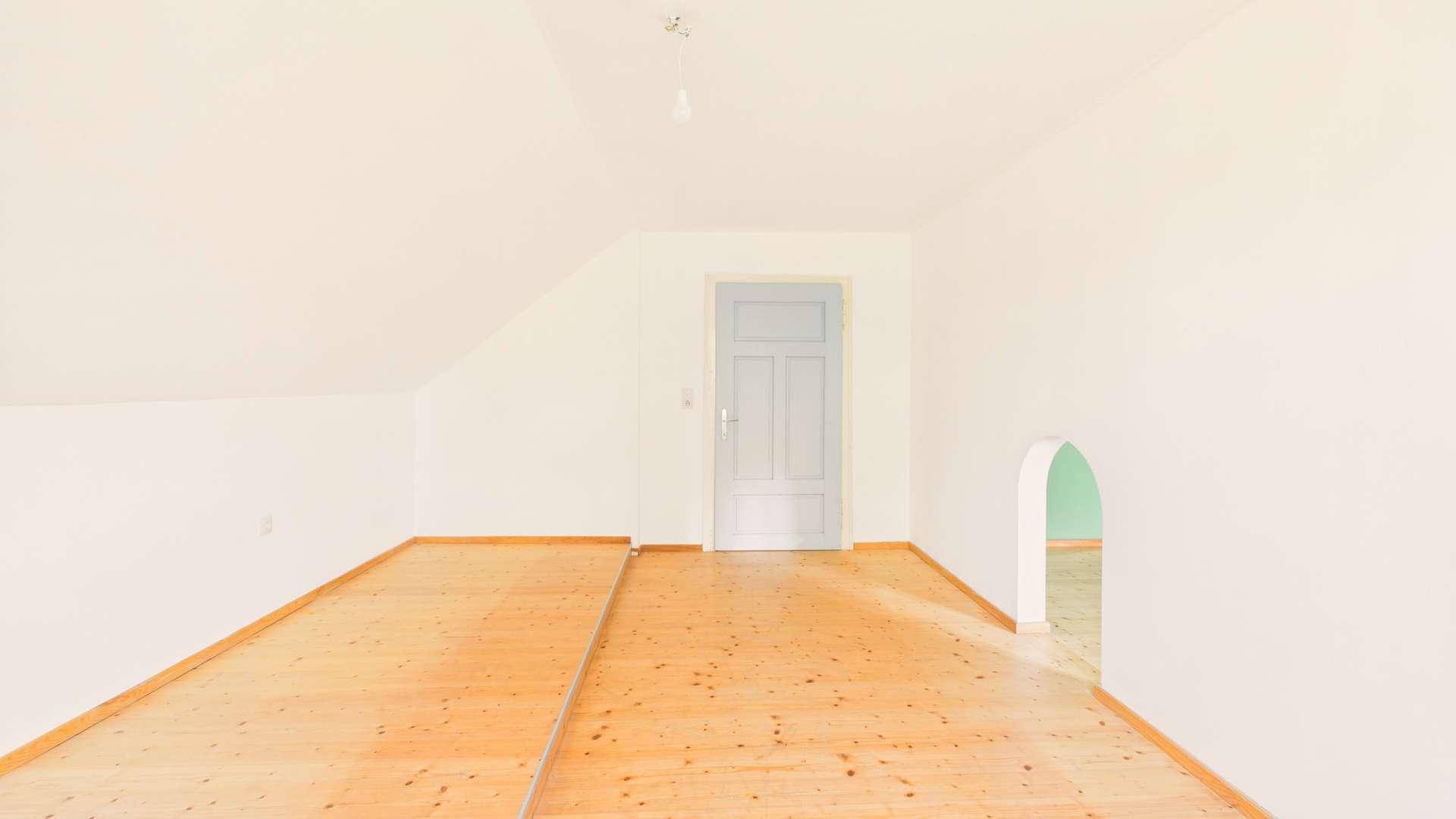Helles Zimmer im Dachgeschoss mit Holzboden und Zugang zu einem weiteren Bereich.
