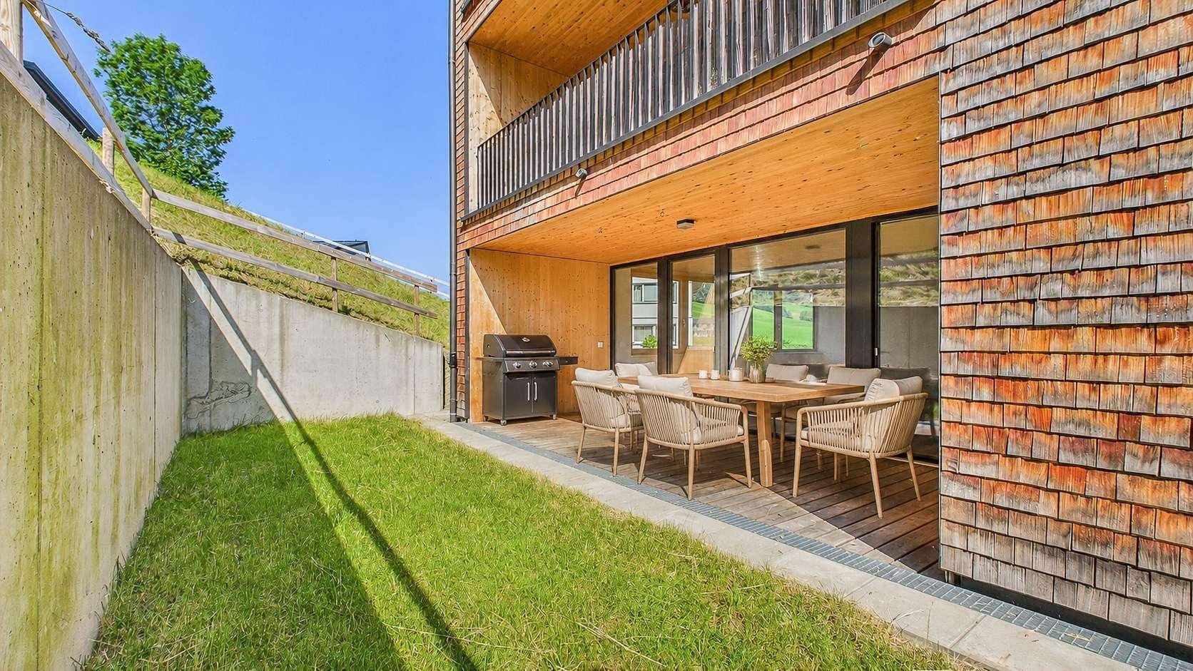Möblierte Terrasse mit Grillplatz und Rasenfläche, ideal für Mahlzeiten im Freien.