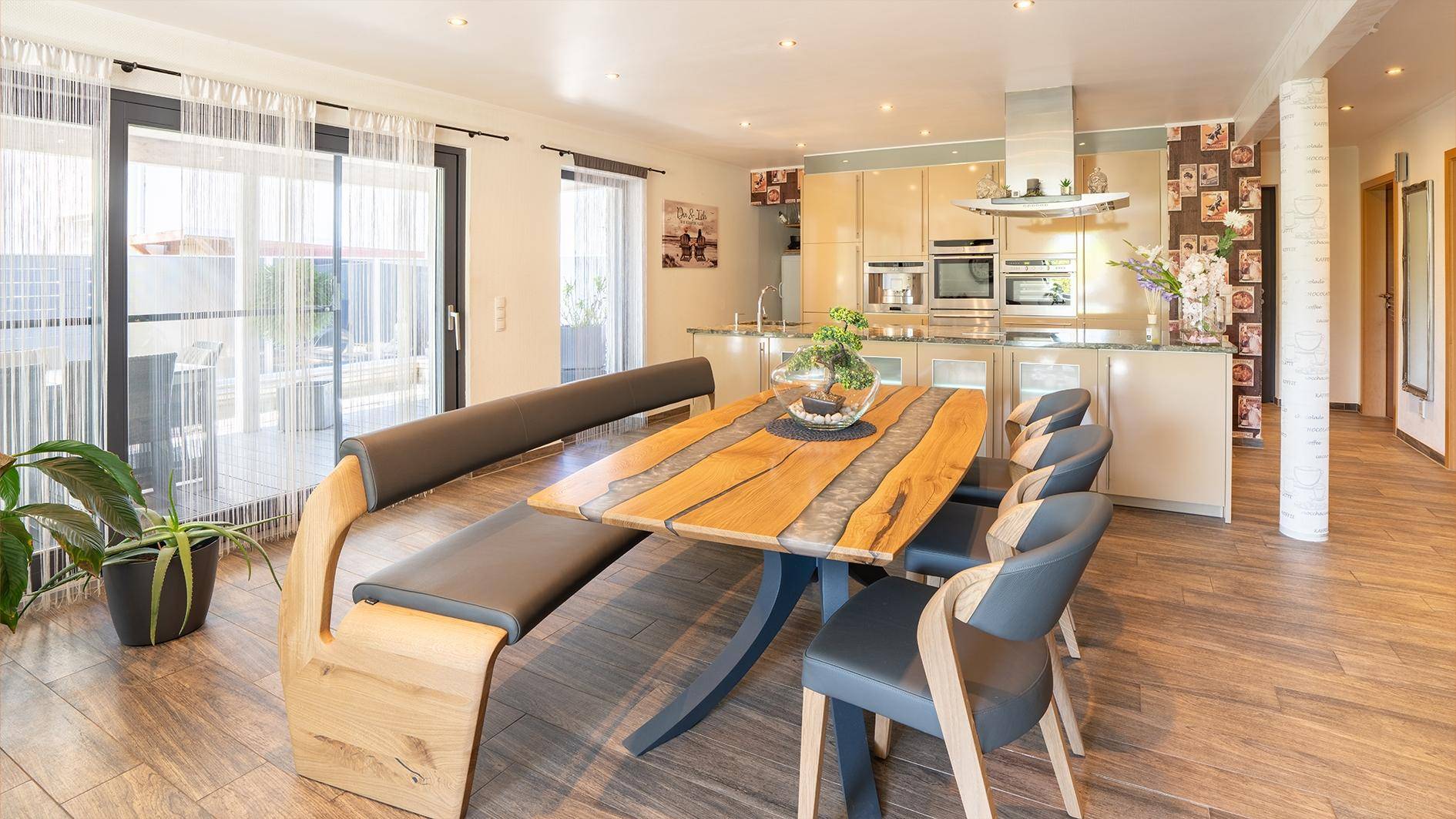 Heller Essbereich mit Holztisch und moderner Küche mit glänzenden Fronten und Premium-Geräten.