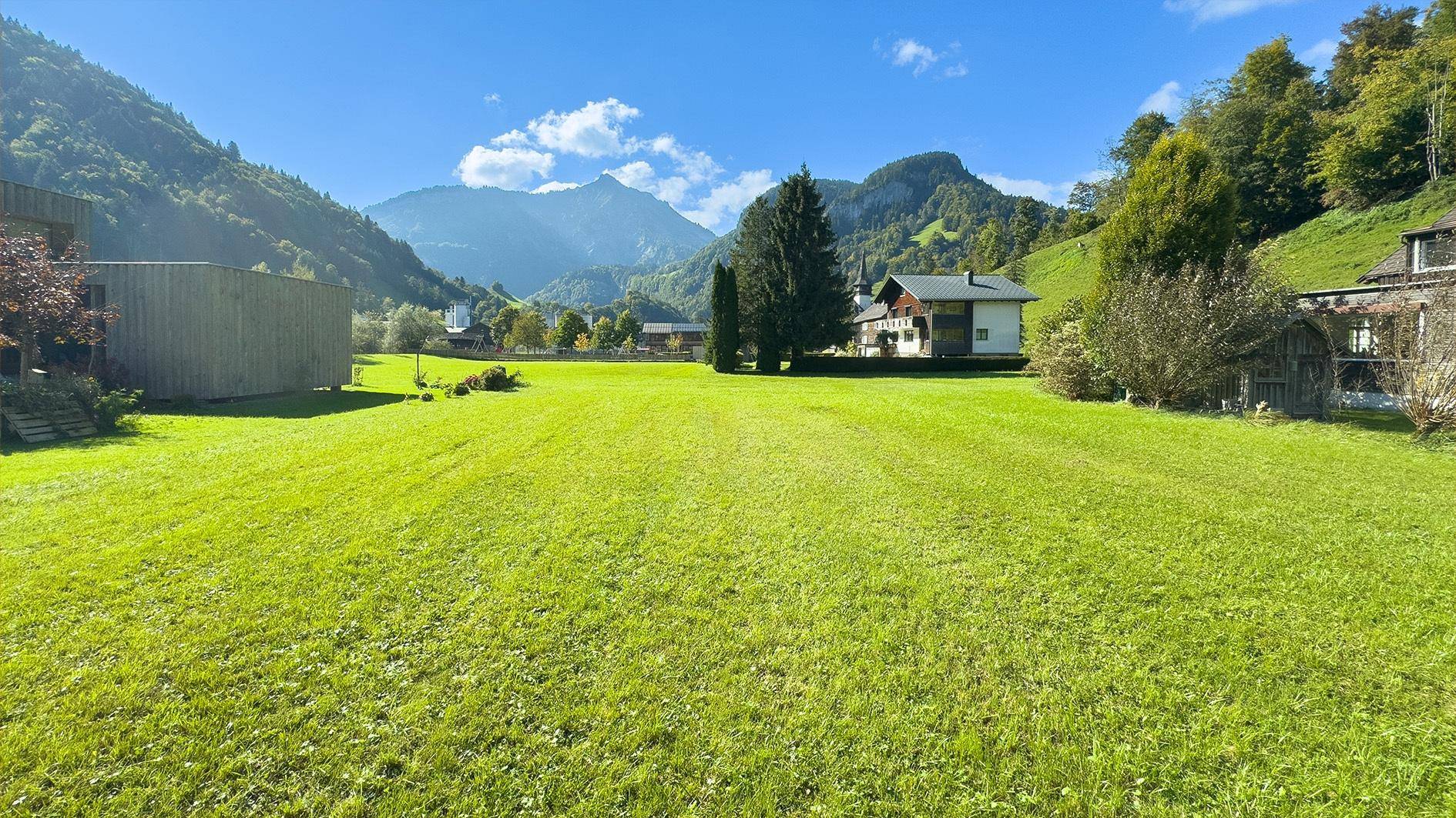 Malerische Landschaft mit weiten Grünflächen und majestätischen Bergen im Hintergrund unter blauem Himmel.
