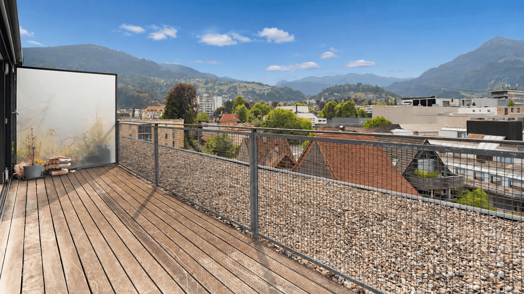 Sonniger Terrassenbereich mit Holzboden, Sichtschutz und weitem Blick über die Stadt und die Berge.