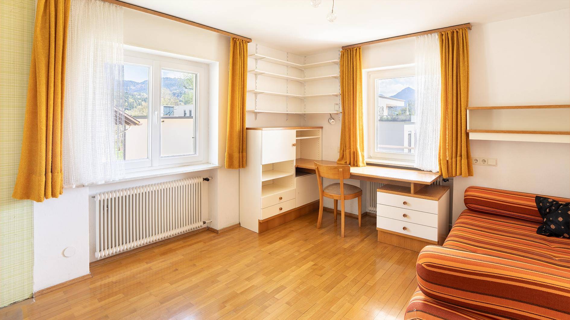 Geräumiges Arbeitszimmer mit viel Tageslicht, Schreibtisch und integrierten Regalen.