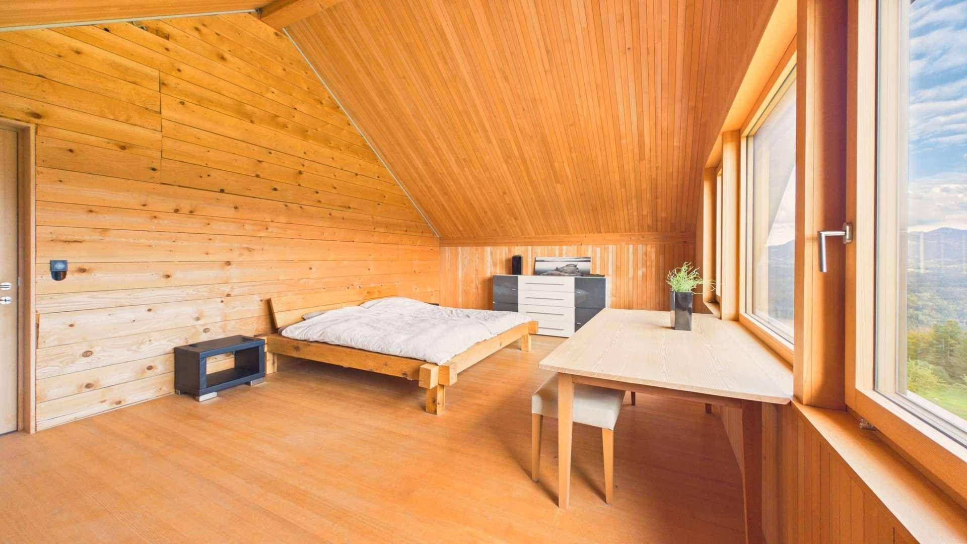 Helles Schlafzimmer im Dachgeschoss mit Holzwänden, Holzboden und großem Fenster mit Bergblick.