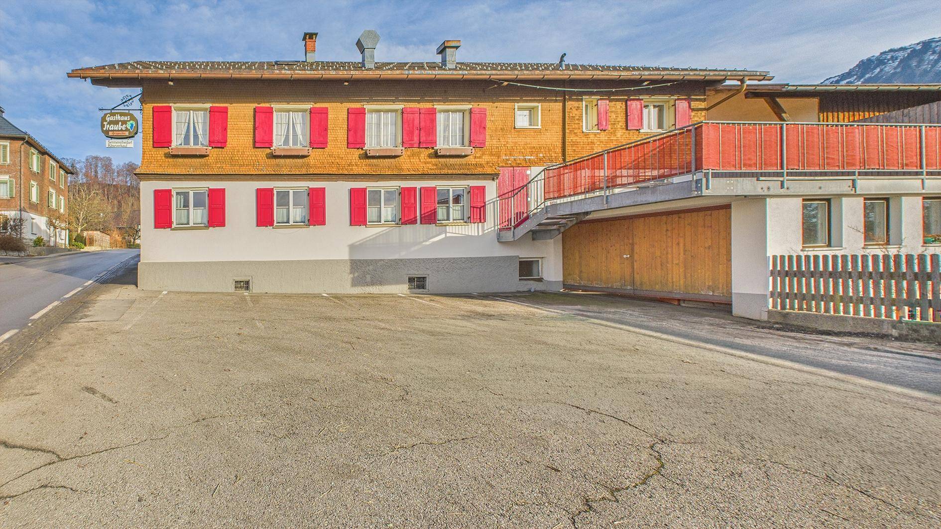 Traditionelles Gasthaus mit roten Fensterläden und großem Parkplatz vor dem Gebäude.