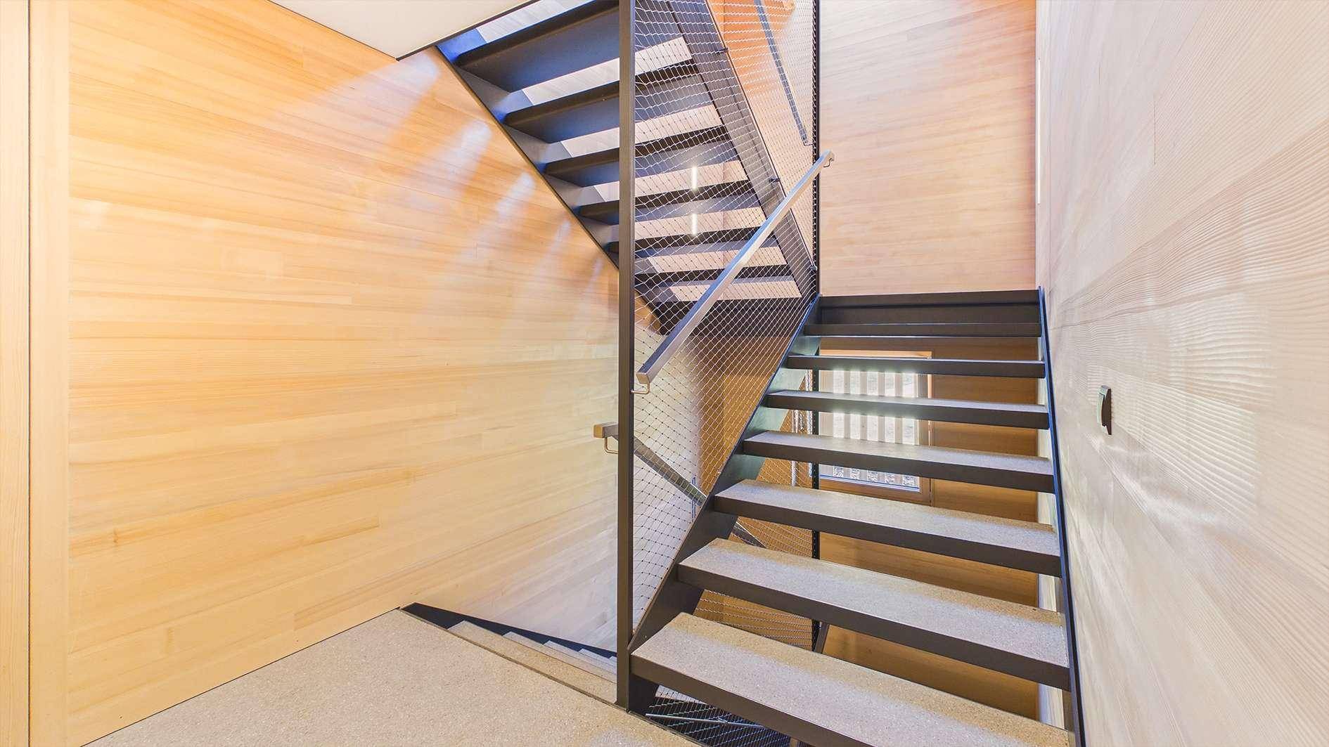 Modernes Treppenhaus mit Holzverkleidung und Metallgeländer, das die Etagen verbindet.