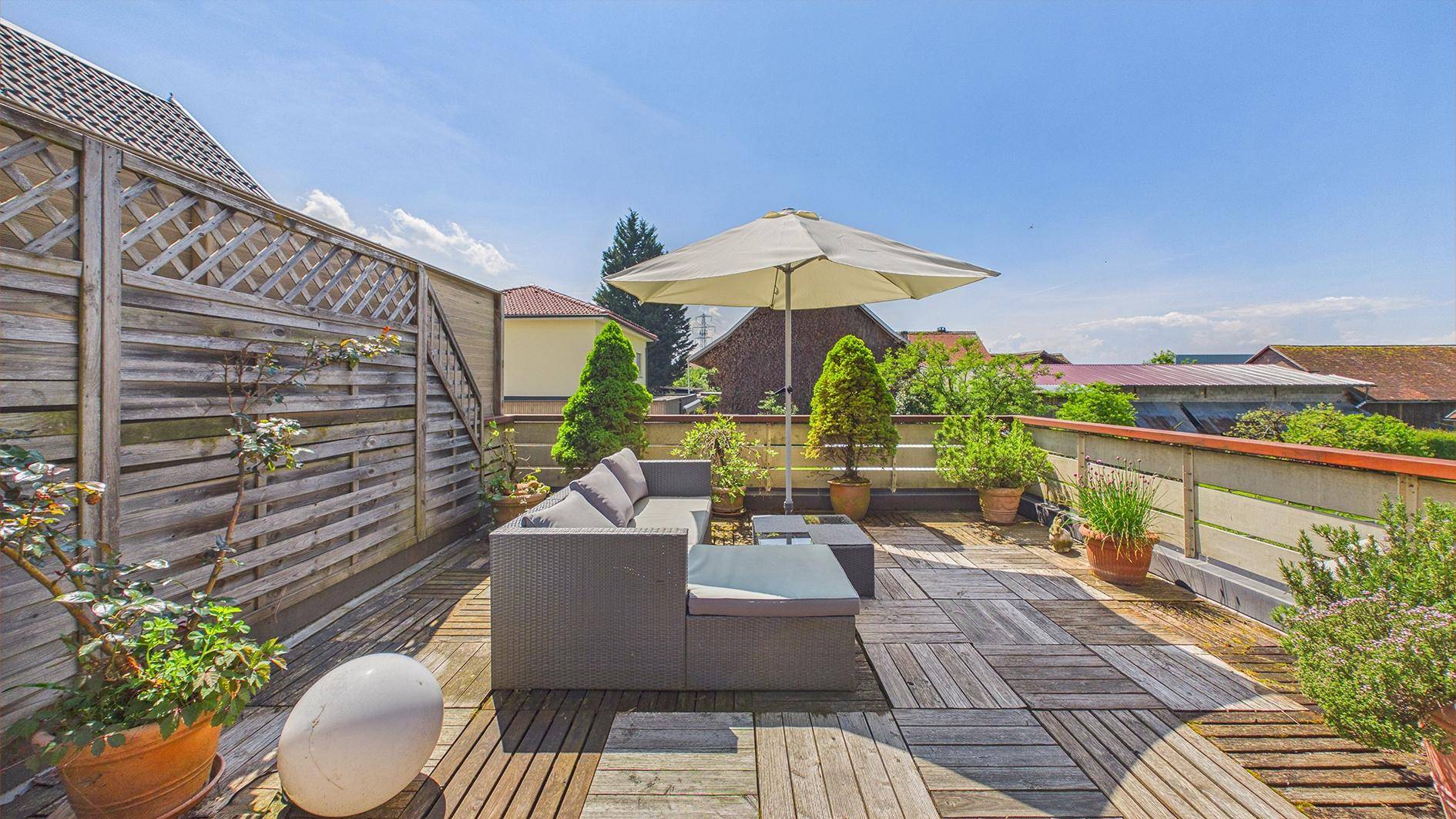 Geräumige Dachterrasse mit Holzfliesen, Lounge-Möbeln und Sonnenschirm für entspannte Stunden.