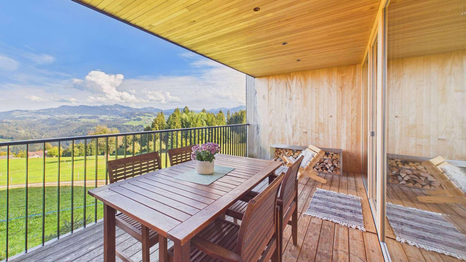Geräumiger Balkon mit Holzboden, Esstisch und Stühlen, bietet einen weiten Blick auf die Berge.