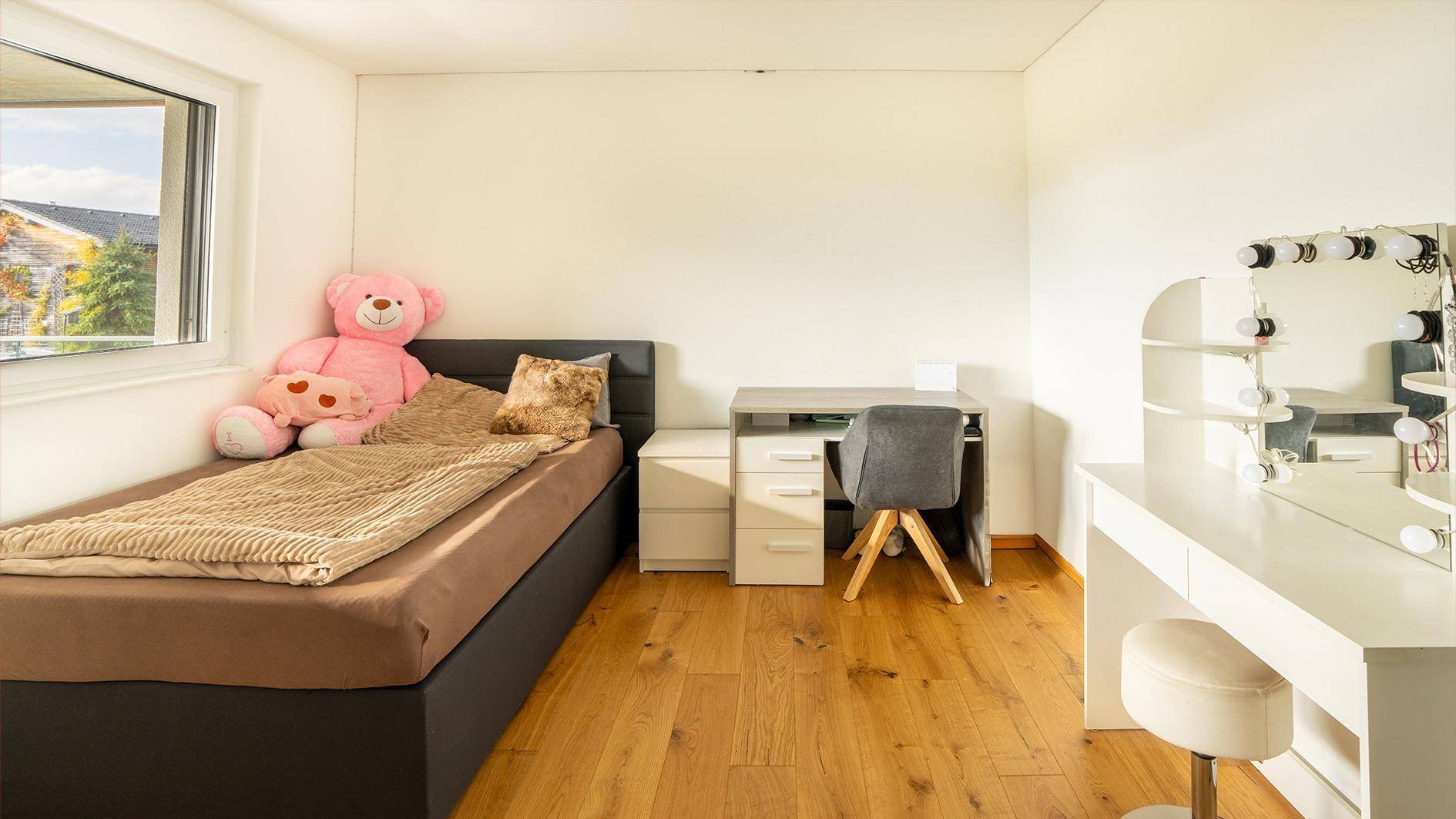 Kinderzimmer mit Einzelbett, Schreibtisch und Schminktisch mit Beleuchtung.