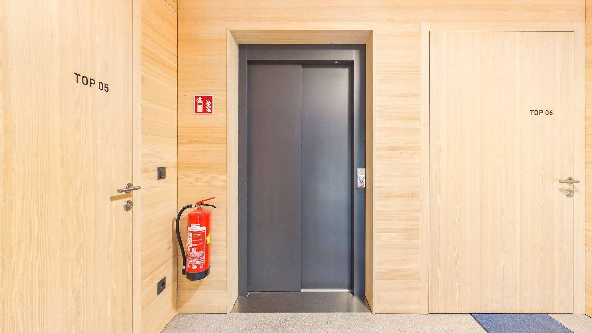 Heller Flur im Gebäude mit Aufzug und Holzwänden, der zu den Wohnungen führt.