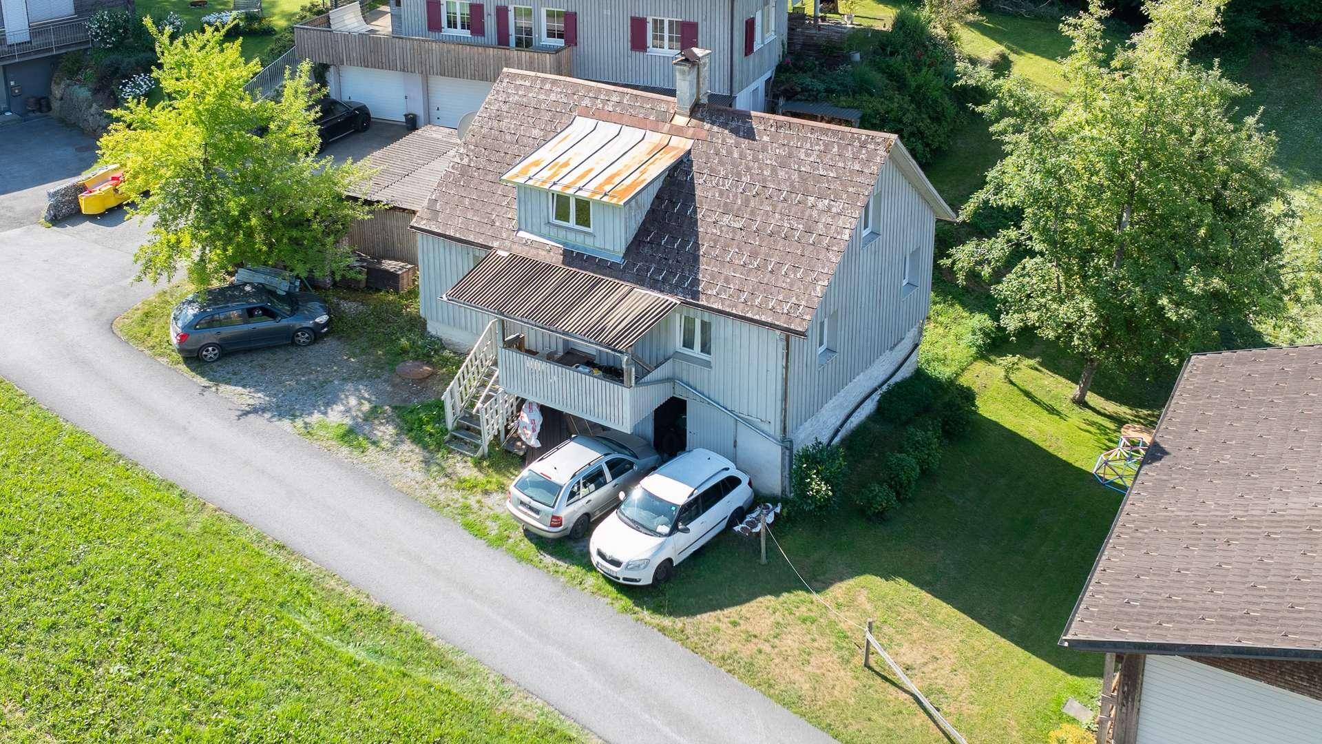 Luftaufnahme des Hauses mit Holzfassade, Satteldach und Parkplätzen im Grünen.