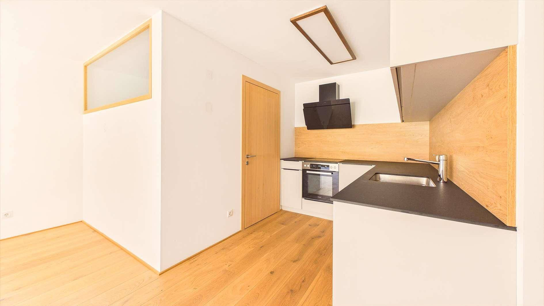 Kompakte, moderne Küche mit weißen Fronten, dunkler Arbeitsplatte und Holzwandverkleidung.