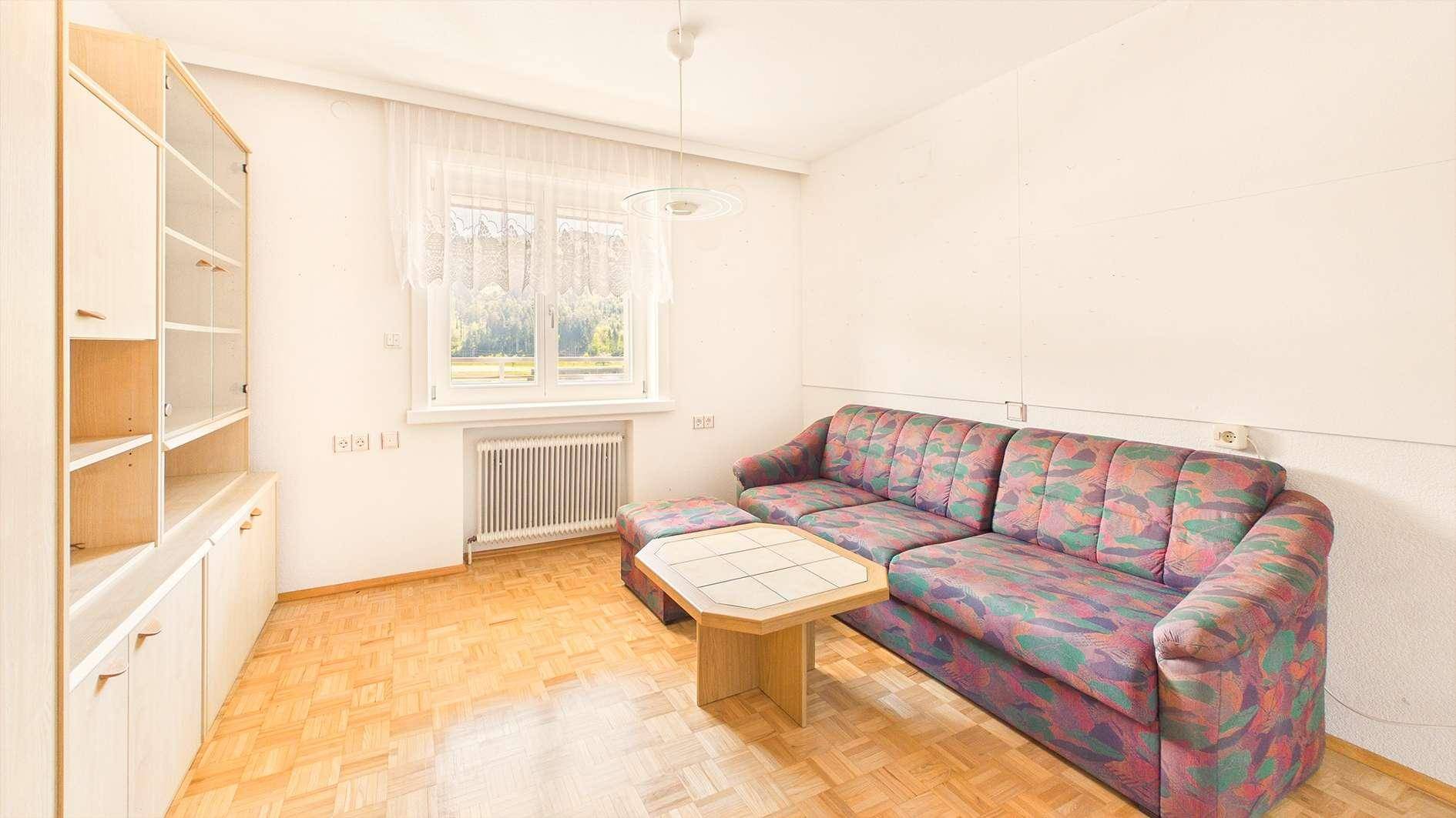 Helles Zimmer mit Parkettboden, Sofa und Fenster mit Blick ins Grüne.