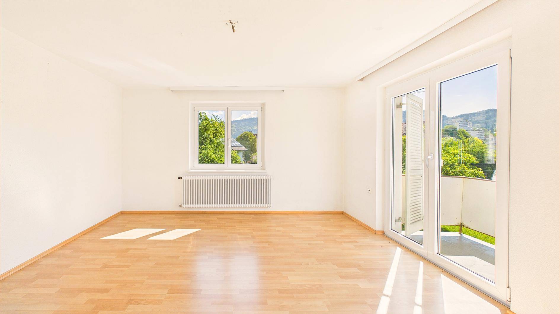 Helles, leeres Zimmer mit Parkettboden und Zugang zu einem Balkon, ideal als Wohnbereich.