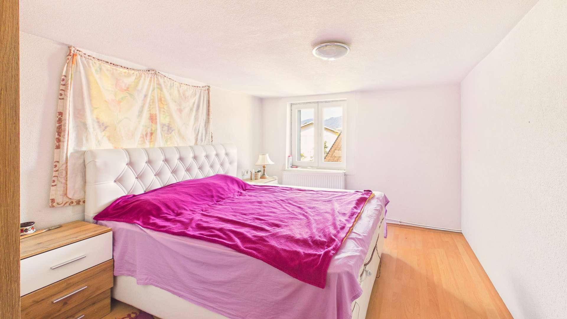 Helles Schlafzimmer mit großem Bett, Holzboden und Fenster mit Blick nach draußen.