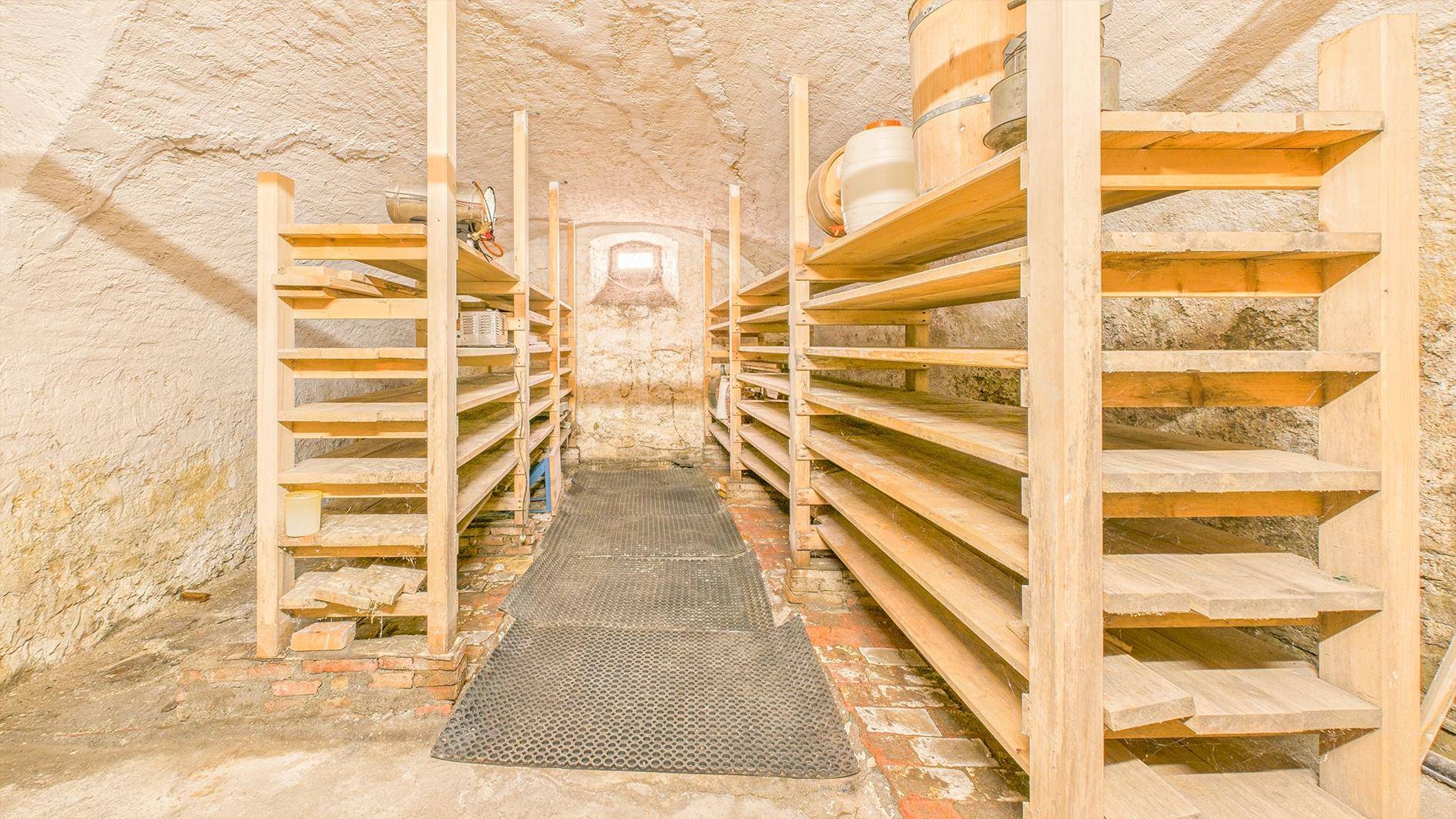 Rustikaler Kellerraum mit Holzböden und Steinwänden, ausgestattet mit Regalen für Lagerung.