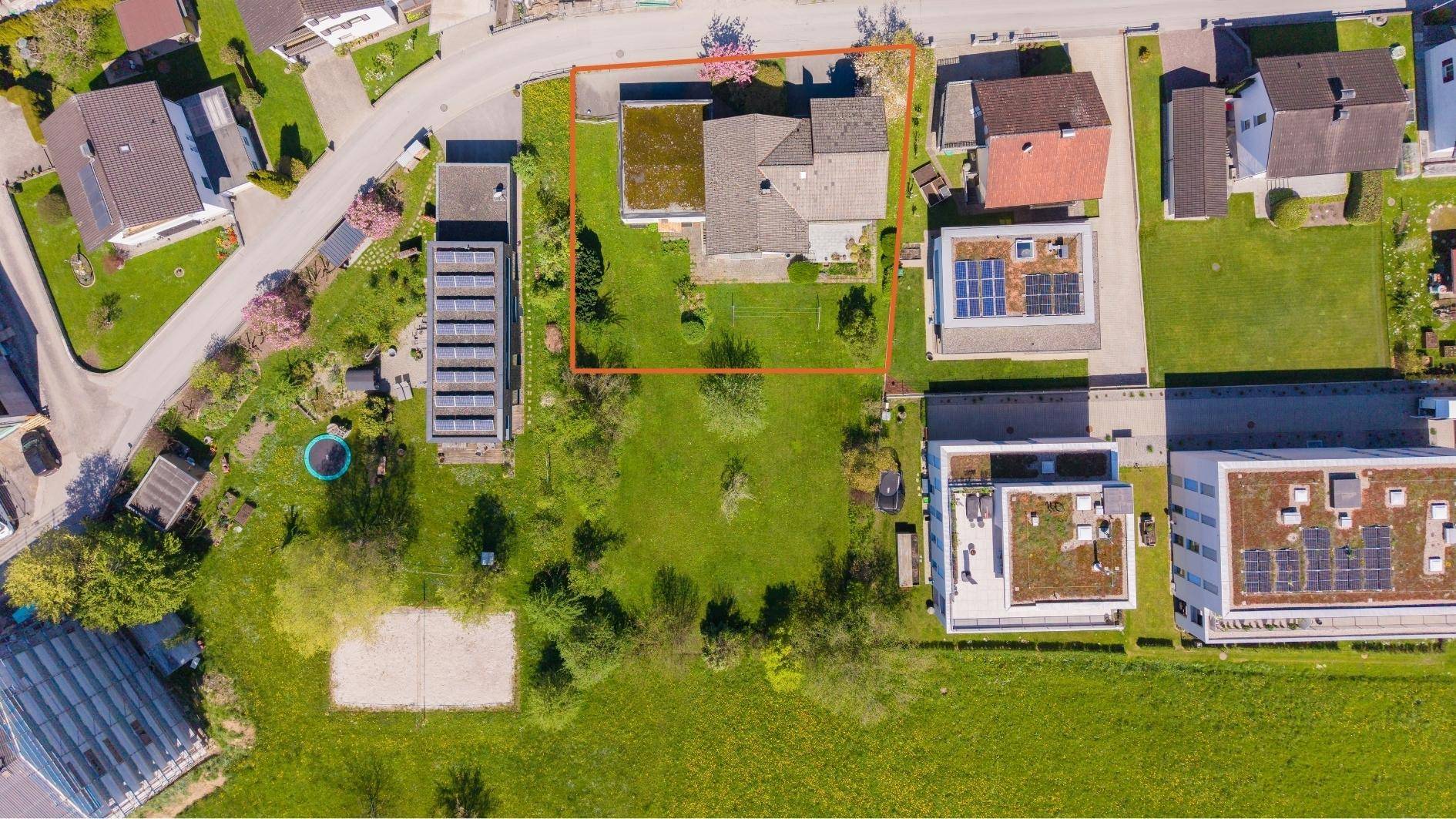 Vogelperspektive eines Grundstücks mit Haus, großem Garten und umliegenden Gebäuden, rot umrandet.