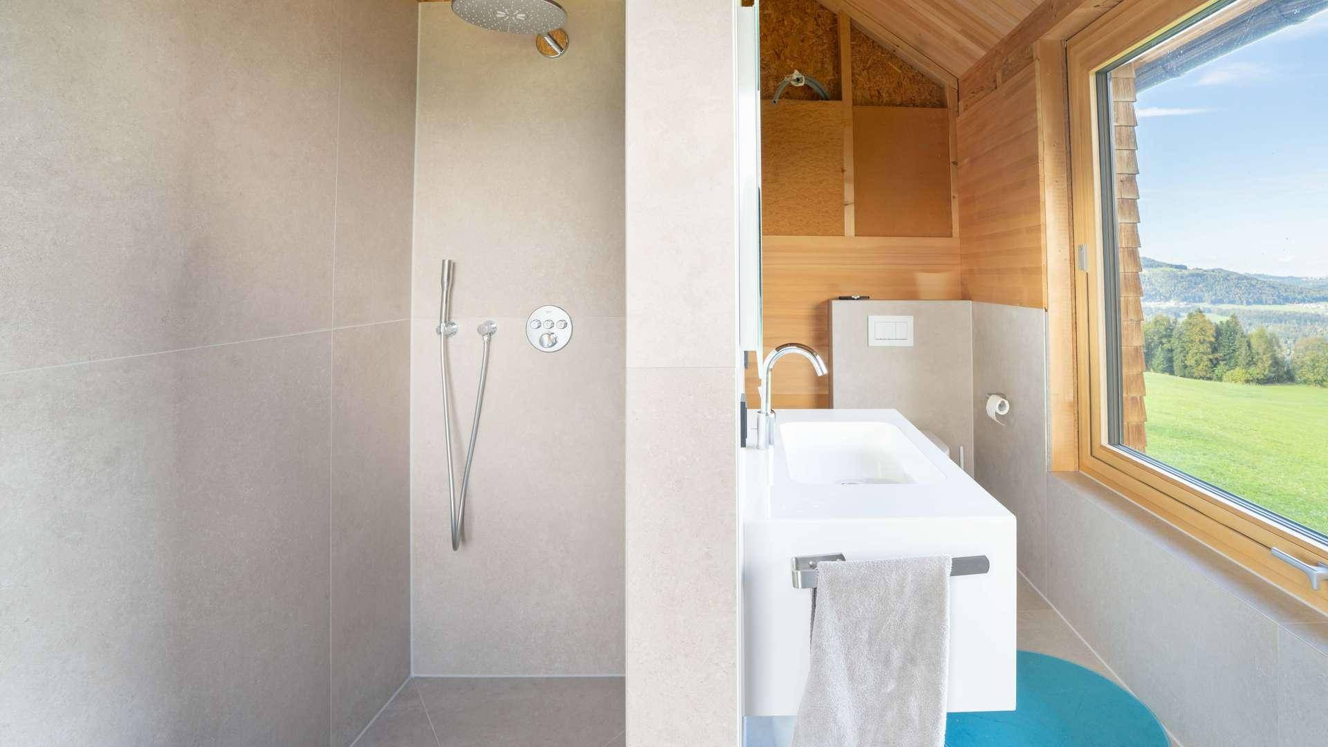 Modernes Badezimmer mit Waschtisch, Dusche und Fenster mit Blick auf die Natur.