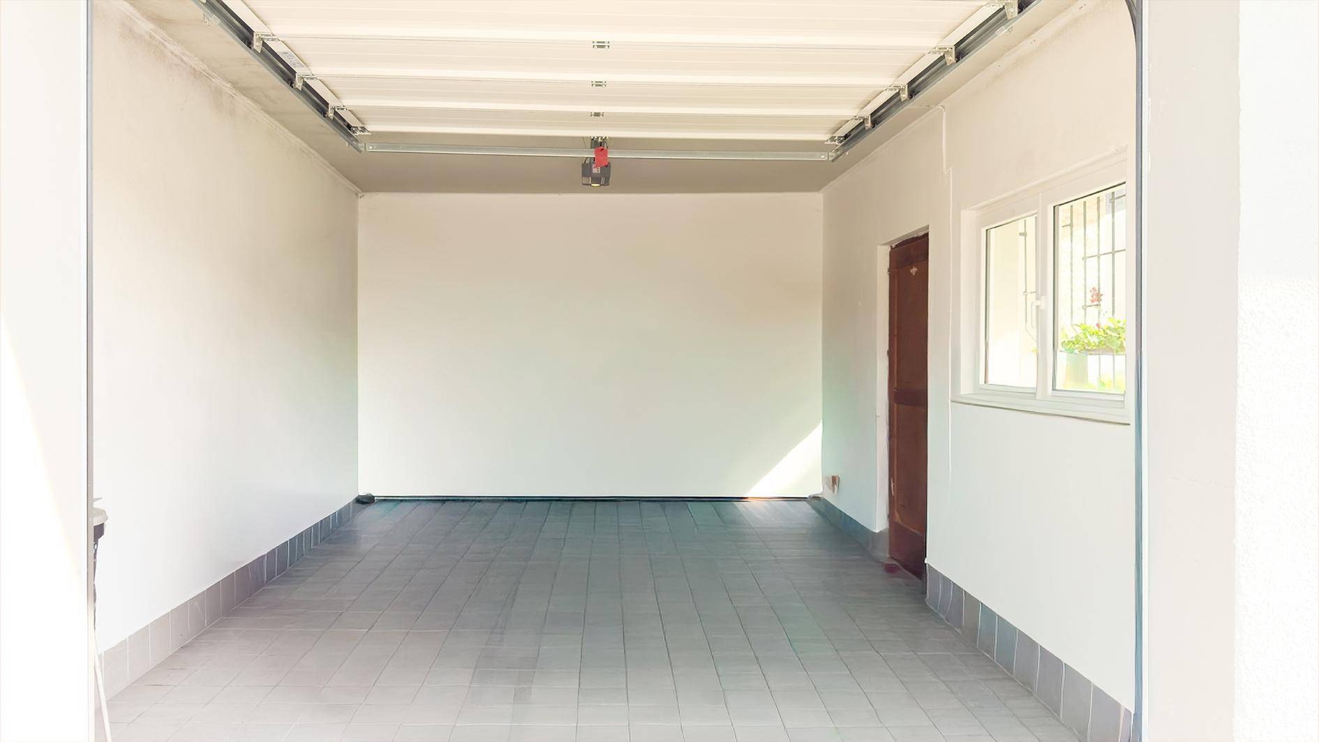 Leere Garage mit gefliestem Boden, weiß gestrichenen Wänden und einem Fenster für Tageslicht.