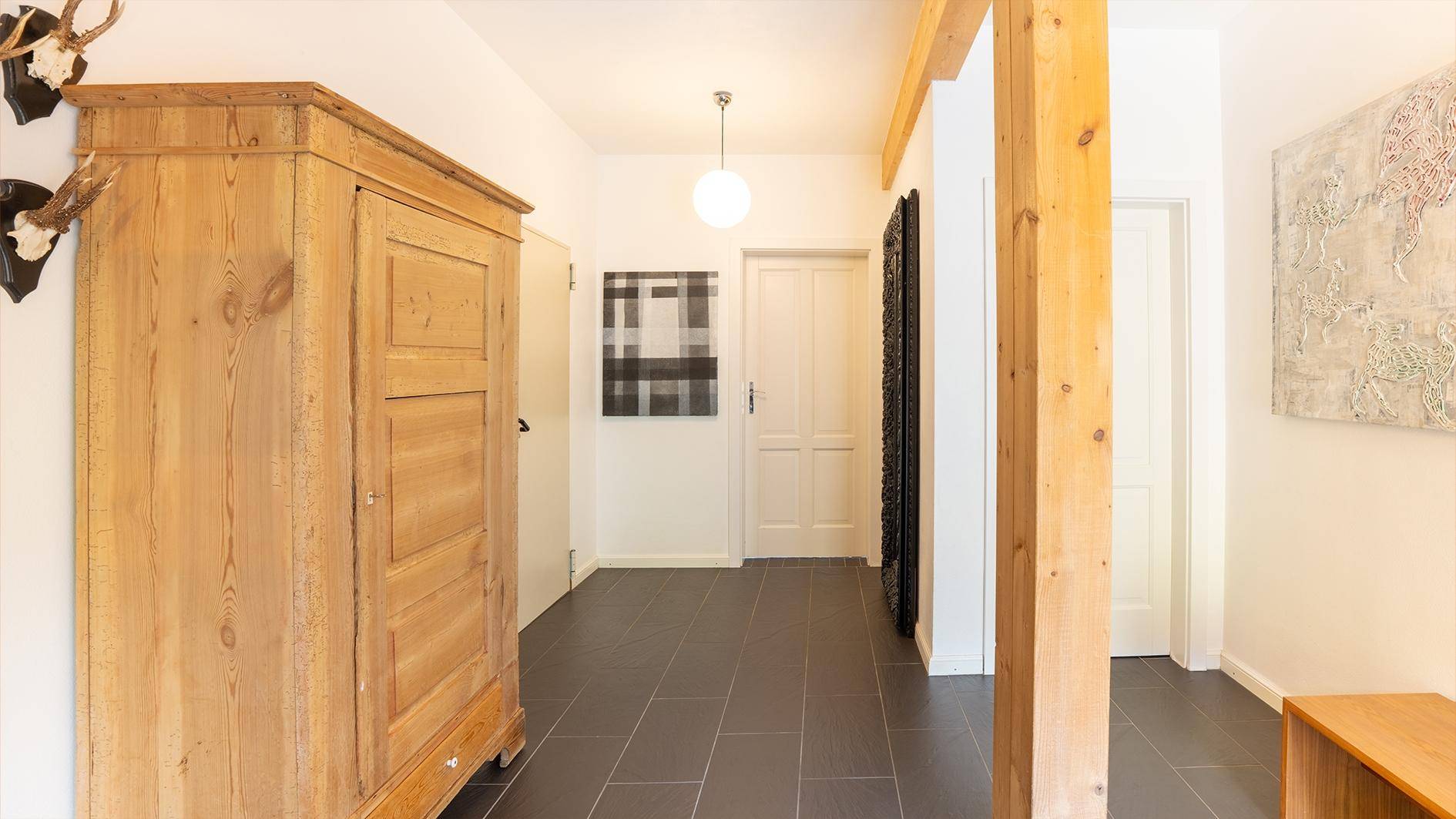 Heller Flur mit dunklem Fliesenboden, Holzbalken und traditionellem Holzschrank.