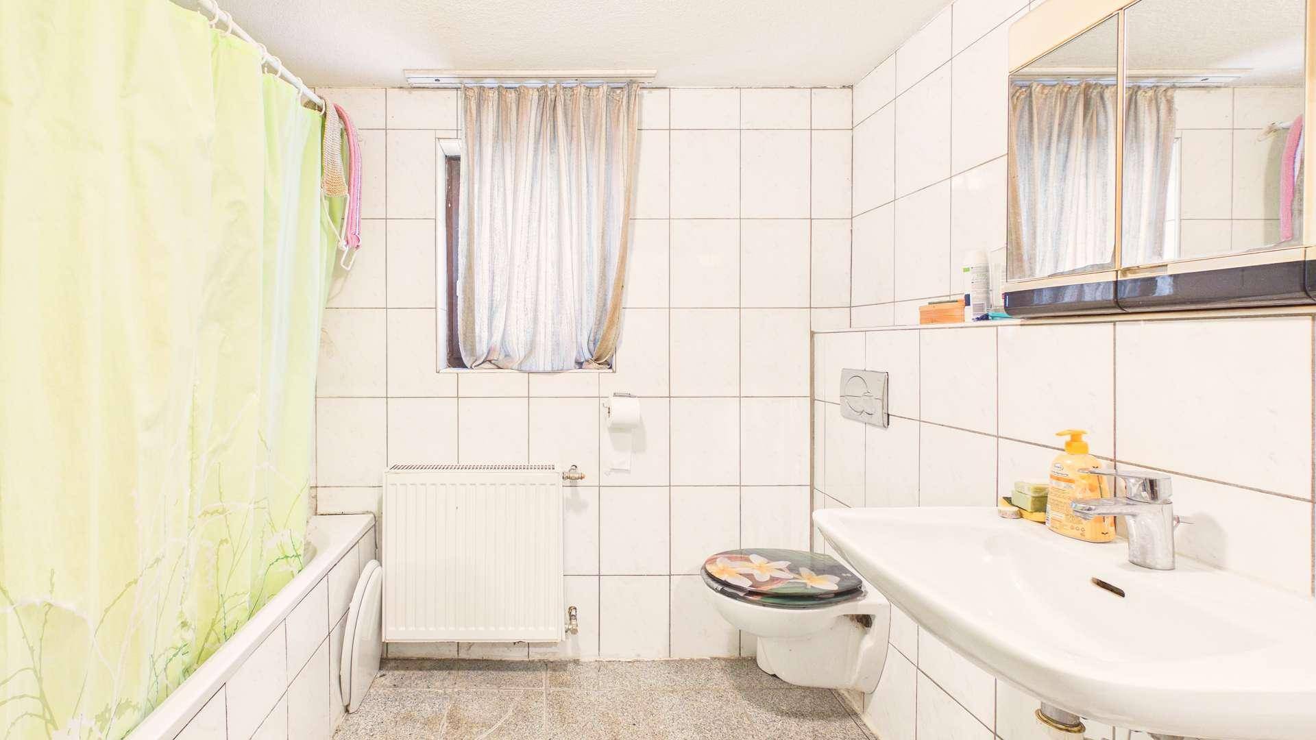 Badezimmer mit weißen Fliesen, Badewanne, WC und Waschbecken sowie einem Fenster.