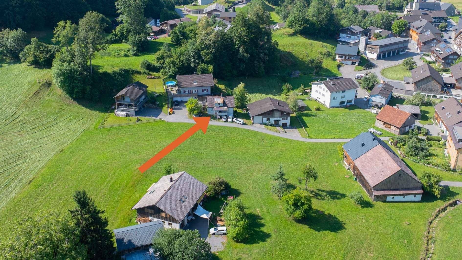 Luftaufnahme eines Hauses mit umliegenden Grünflächen und Nachbargebäuden in ländlicher Umgebung.