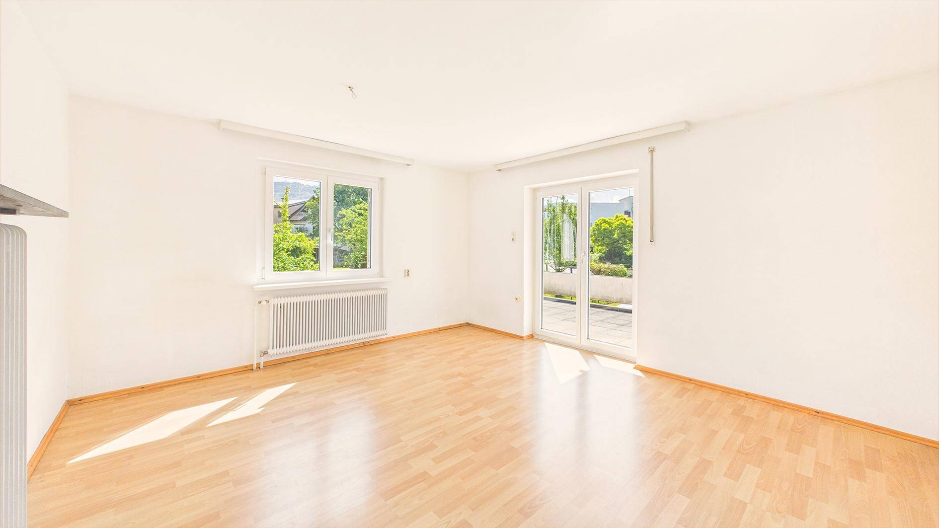 Helles, leeres Zimmer mit Parkettboden und Zugang zu einer Terrasse, ideal als Wohnbereich.