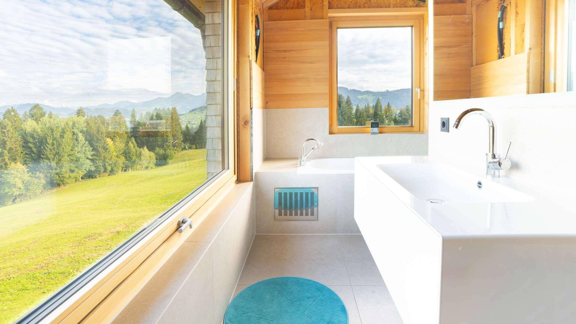 Helles Badezimmer mit Waschtisch, großen Fenstern und Panoramablick auf die grüne Landschaft.