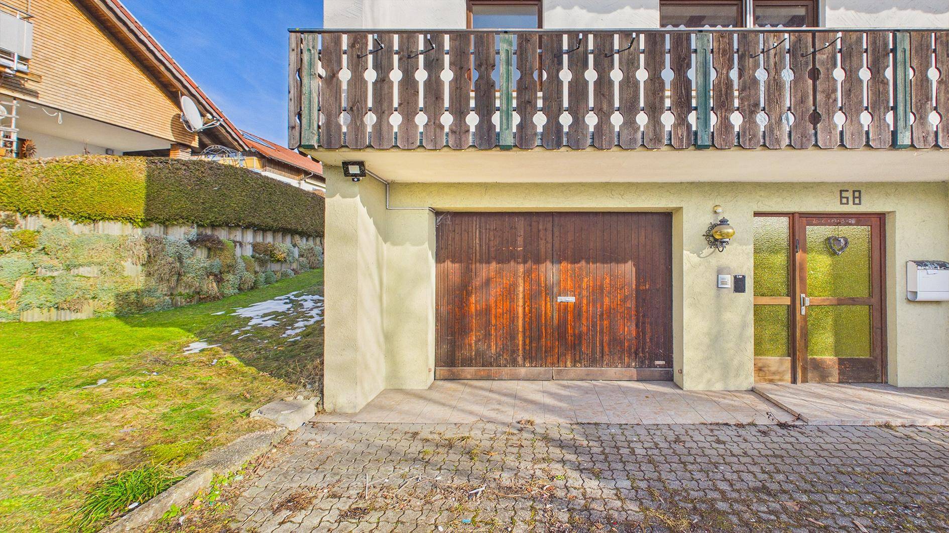 Eingangsbereich des Hauses mit Holzgaragentor und Haustür, umgeben von Grünflächen.