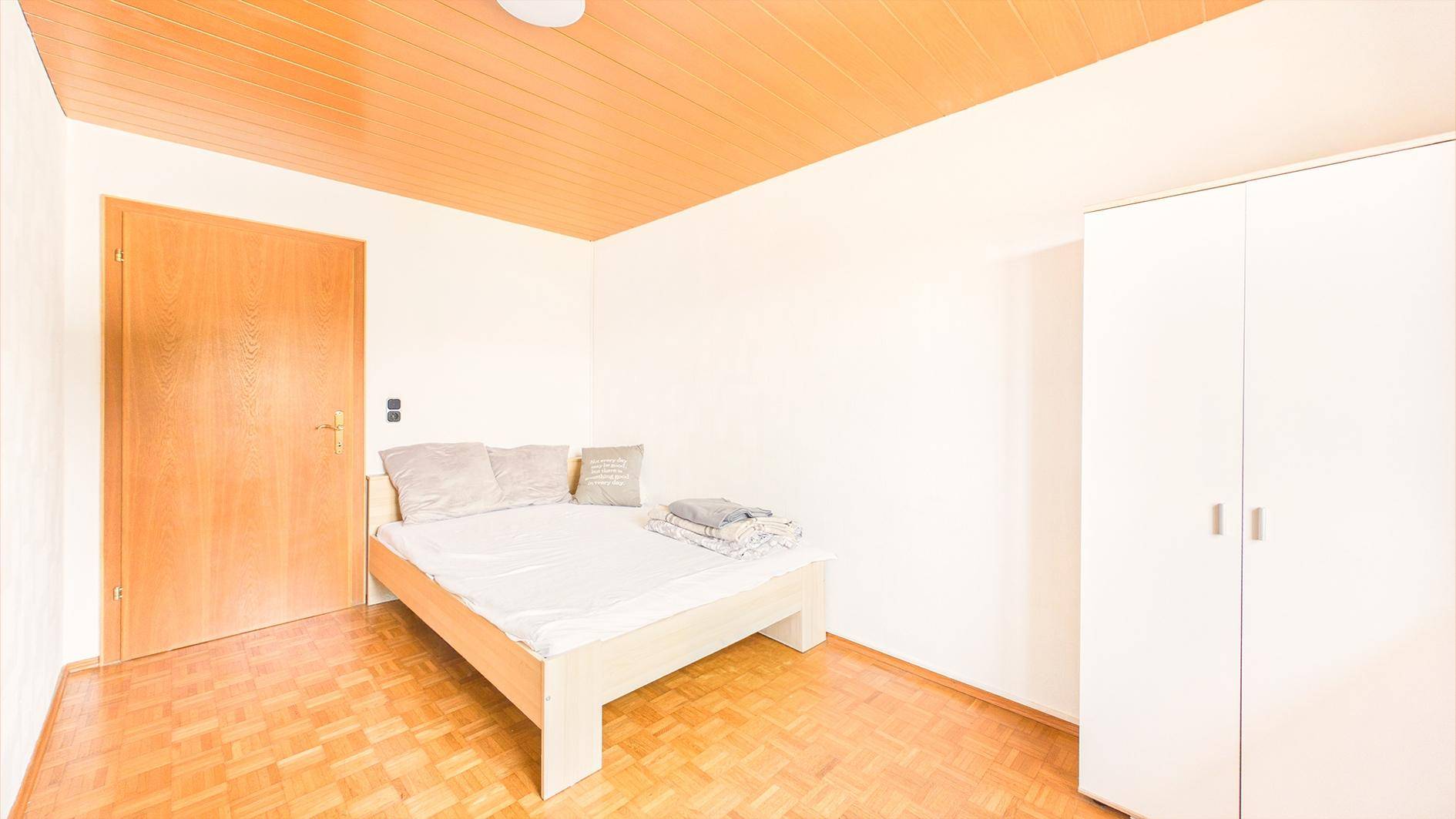 Gemütliches Schlafzimmer mit Parkettboden, Holztäfelung an der Decke und weißem Kleiderschrank.