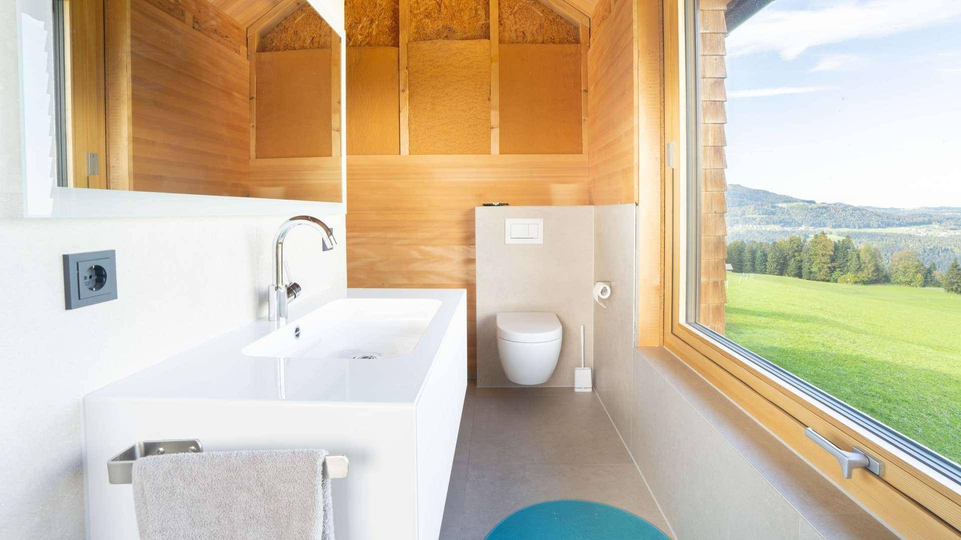 Modernes Badezimmer mit Waschbecken, Toilette und großem Fenster mit weitem Blick ins Grüne.