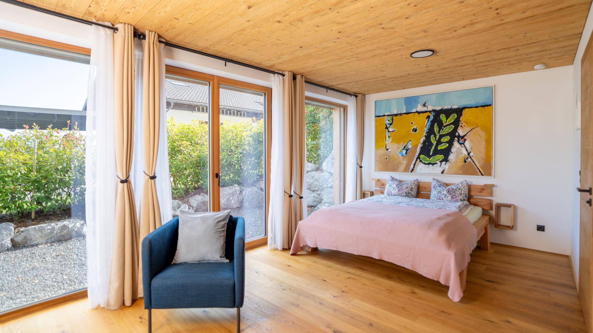 Helles Schlafzimmer mit Holzboden, großem Fenster und direktem Zugang zum Außenbereich.
