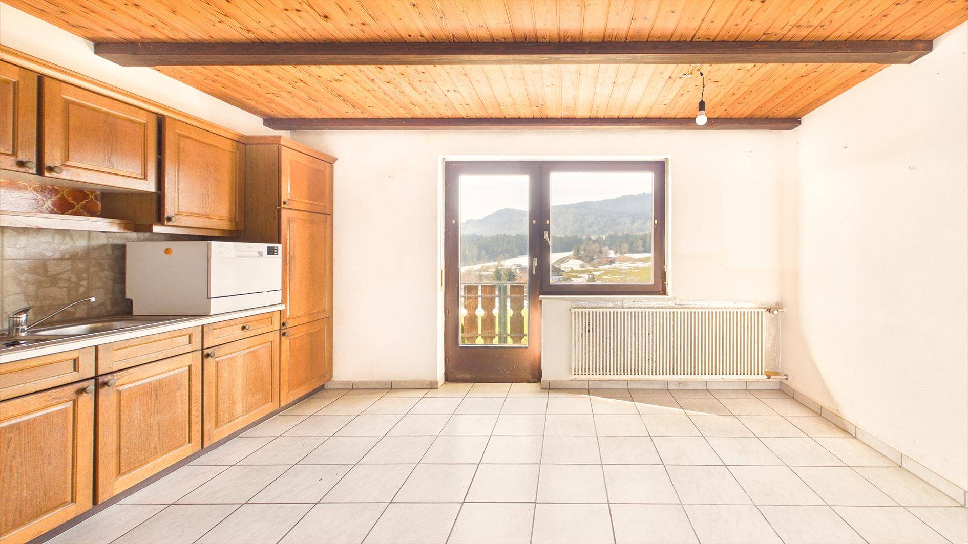 Helle Küche mit Holzdecke, Fliesenboden und Fenster mit Bergblick, inklusive Heizkörper.