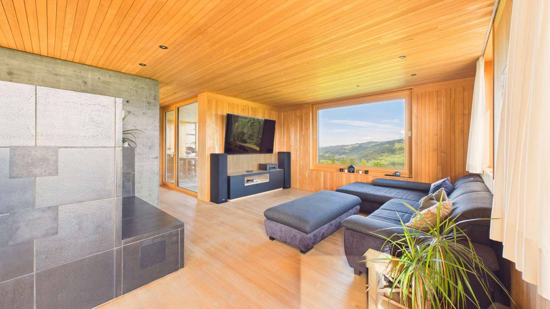 Helles Wohnzimmer mit Holzboden, großem Fenster und Blick auf die umliegende Natur.