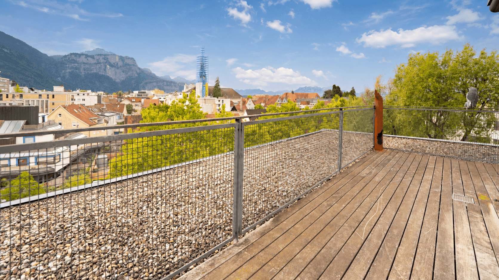 Geräumige Dachterrasse mit Holzboden, Metallgeländer und weitem Blick über die Stadt und Berge.