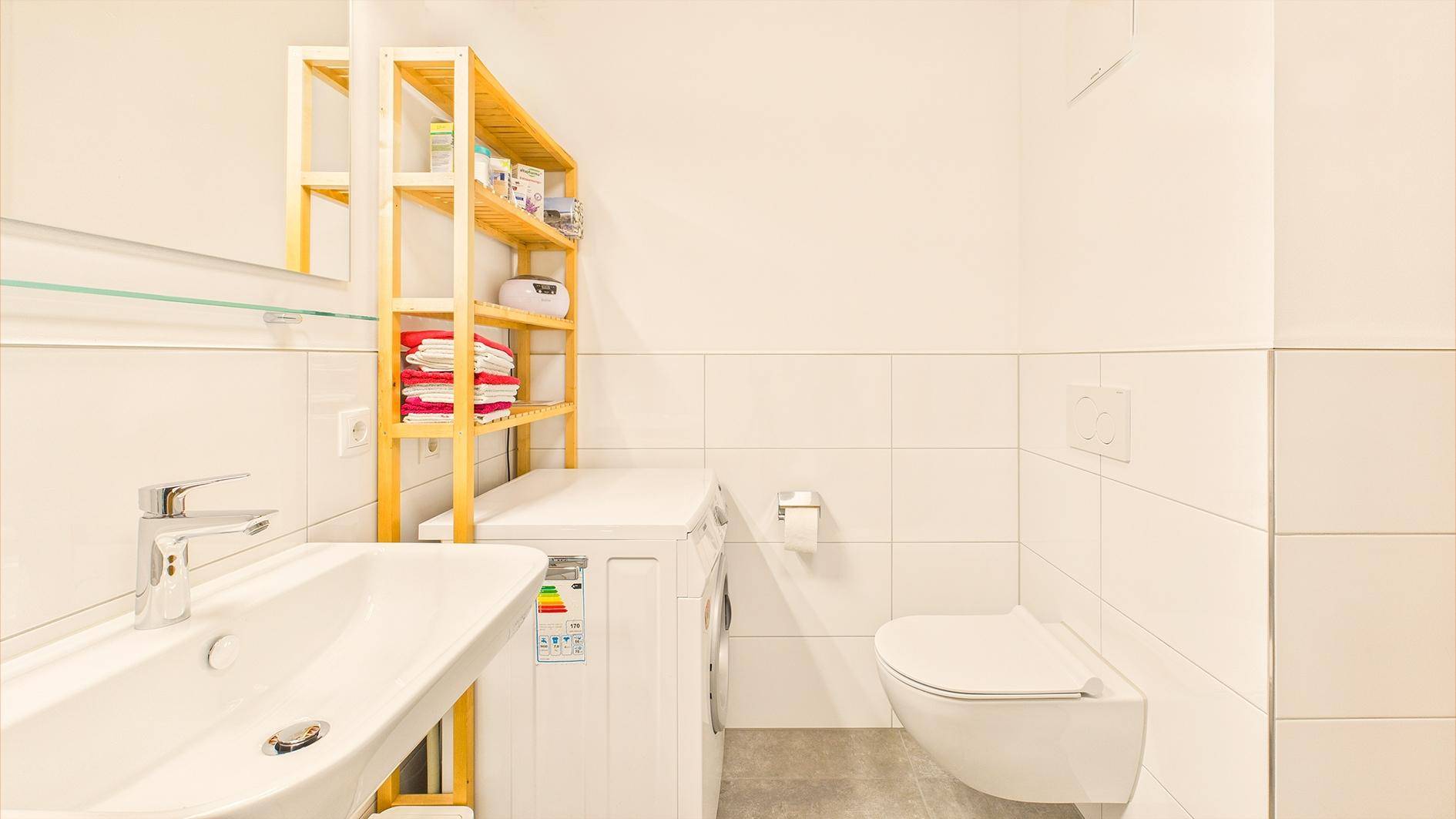 Helles Badezimmer mit Waschbecken, WC, Waschmaschine und Regal für Handtücher.