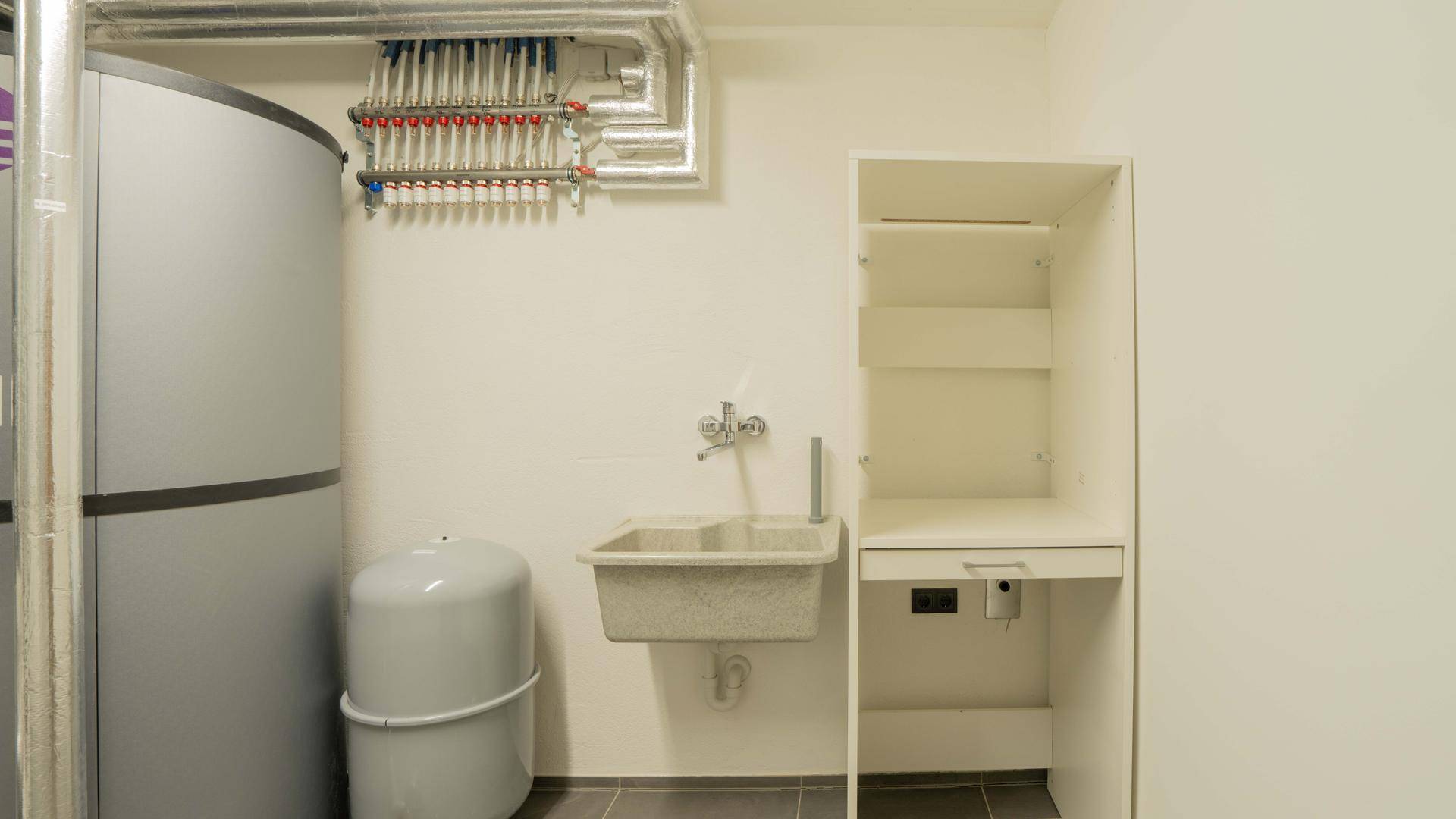 Hauswirtschaftsraum mit Warmwasserspeicher, Heizungsverteiler und Waschbecken.