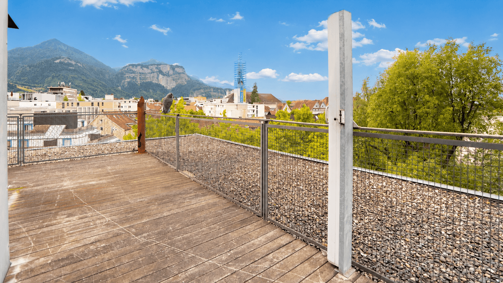 Weitläufige Dachterrasse mit Holzdielen und Panoramablick auf die umliegende Berglandschaft und Stadt.