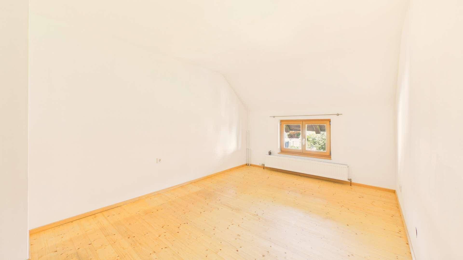 Helles Schlafzimmer im Dachgeschoss mit Holzboden und einem Fenster mit Blick ins Grüne.