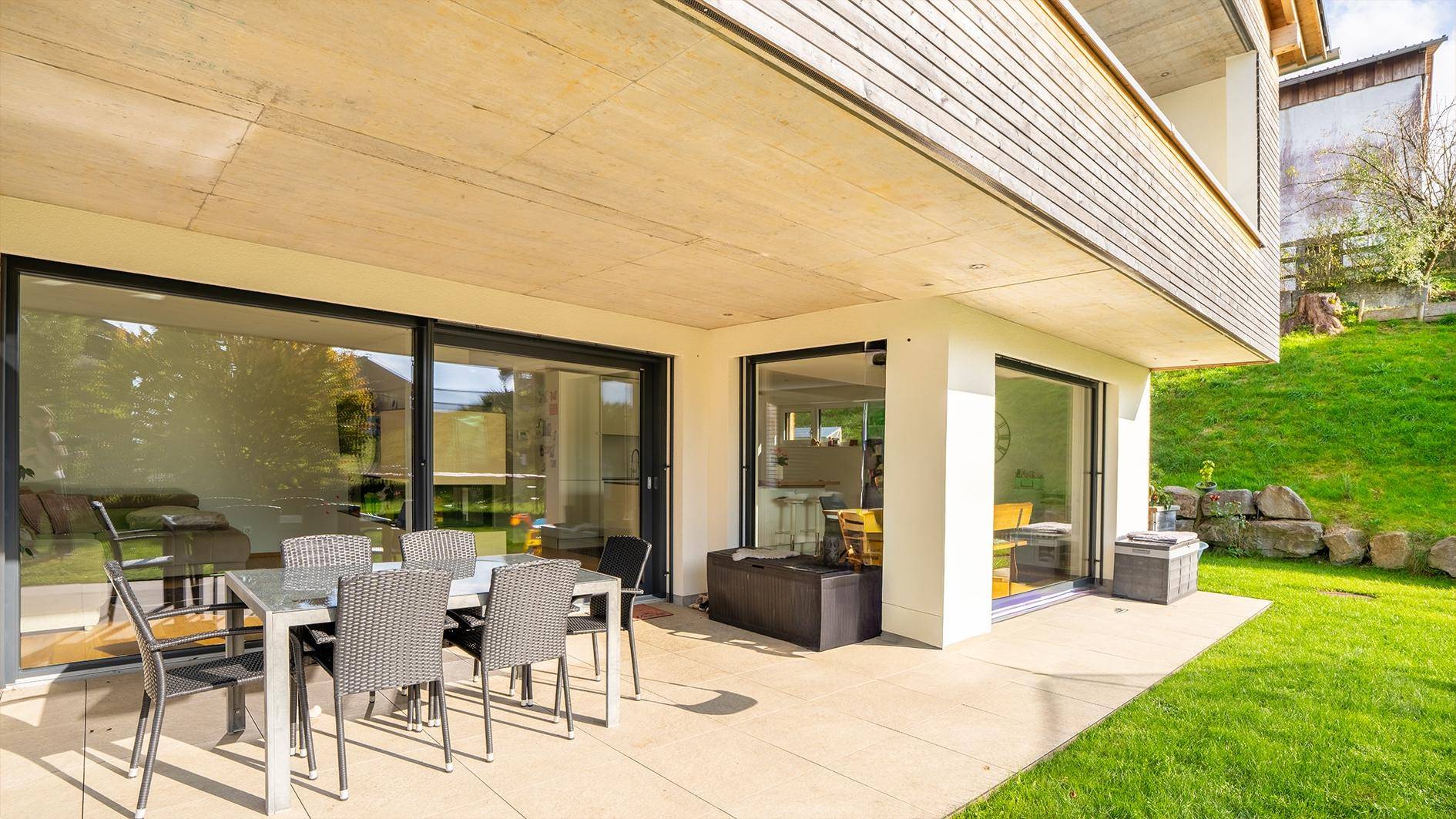 Große, überdachte Terrasse mit Esstisch und Stühlen, direkt am grünen Garten gelegen.
