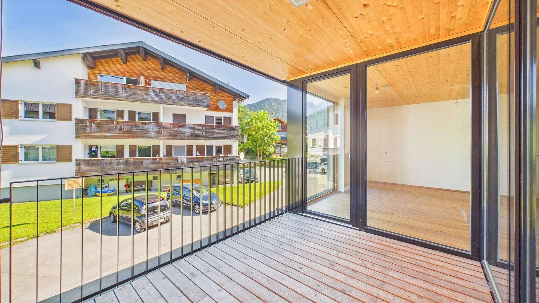 Heller Balkon mit Holzboden und Blick auf den Innenhof sowie die umliegenden Gebäude.