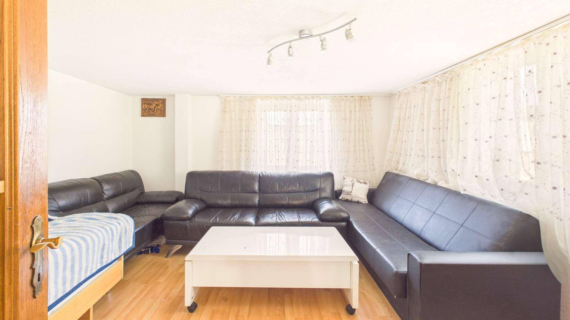 Gemütliches Wohnzimmer mit dunklen Ledersofas, hellem Holzboden und Vorhängen.