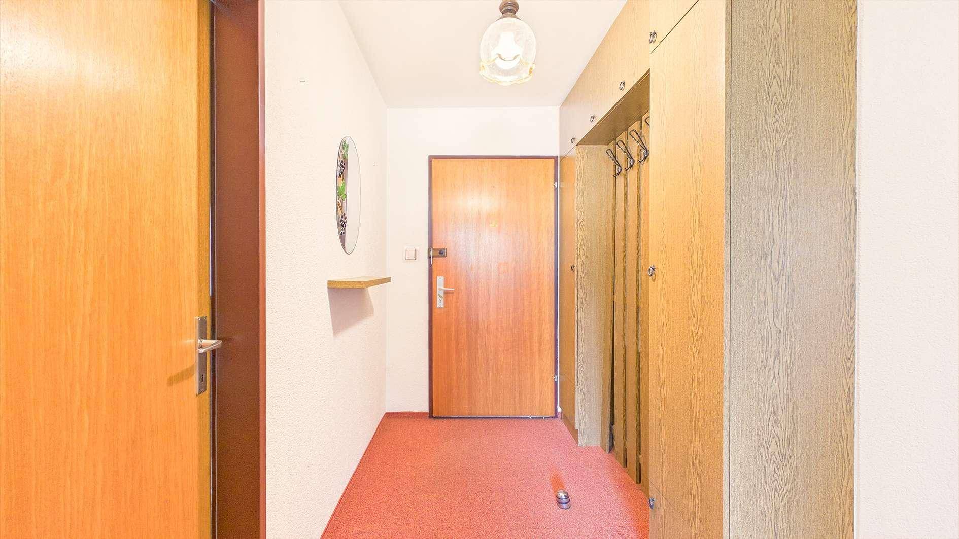 Eingangsbereich mit Teppichboden, Garderobe und Holztür.