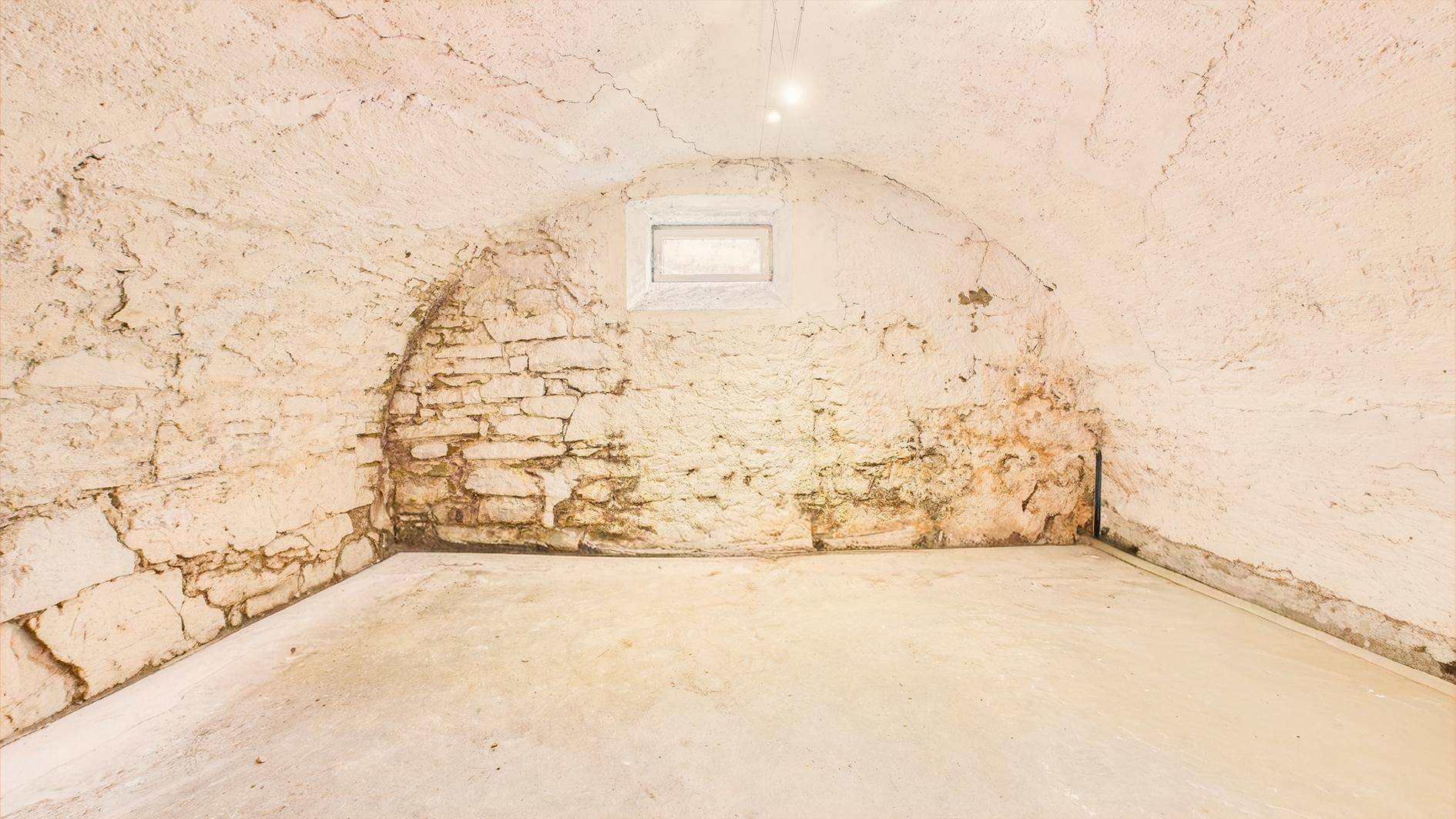 Gewölbekeller mit freiliegenden Steinwänden und einem kleinen Fenster, ideal für Lagerung.