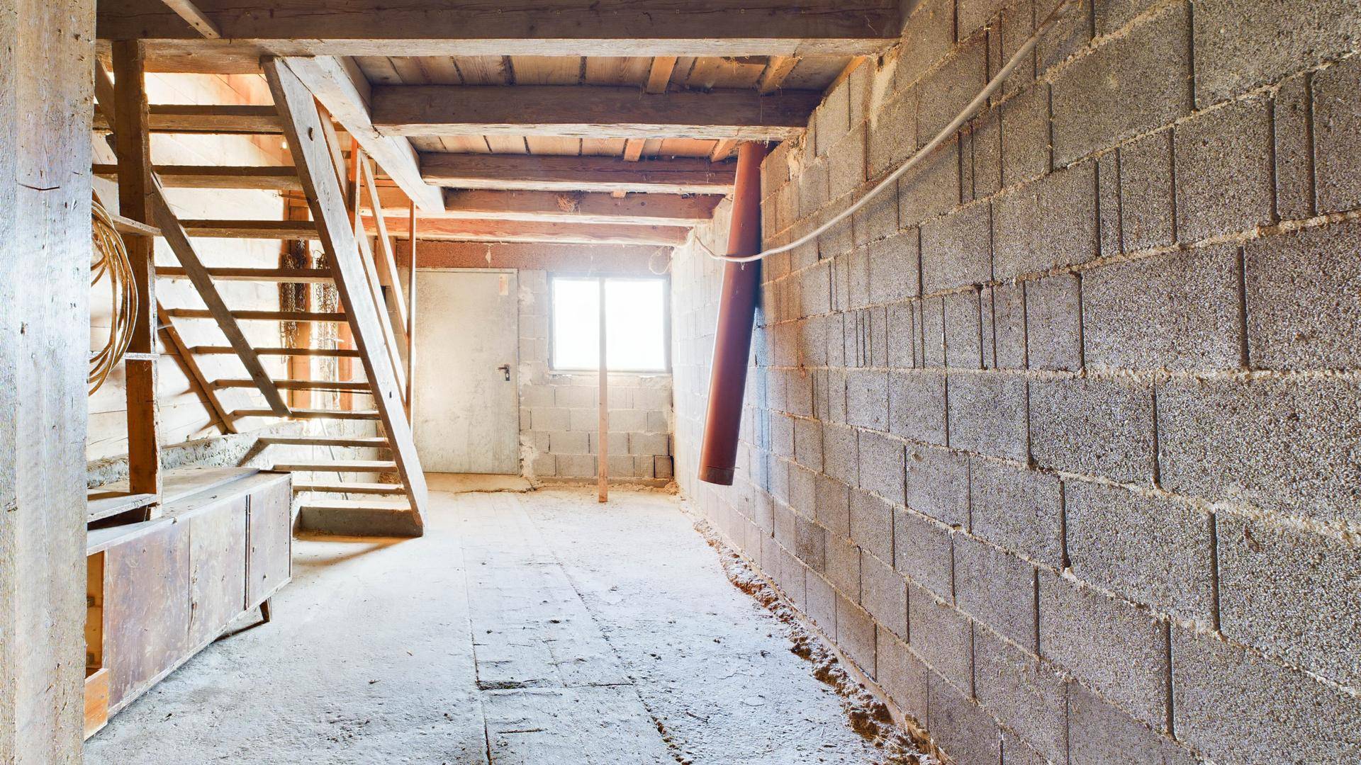 Kellerraum mit Betonsteinwänden, Holztreppe und kleinem Fenster, als Lagerfläche nutzbar.