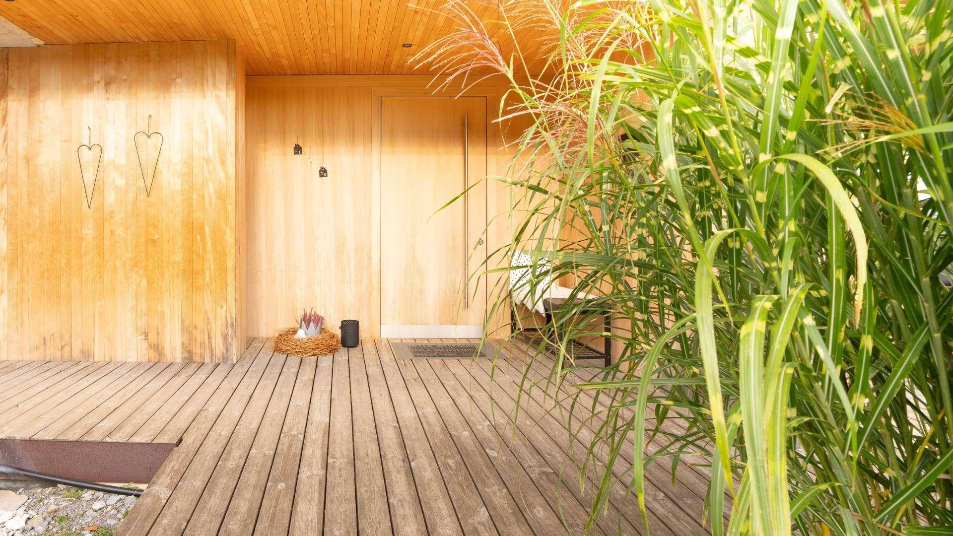 Holzterrasse vor dem Eingangsbereich mit hohen Gräsern und moderner Holzfassade.
